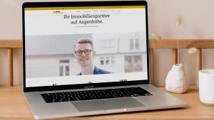 Dieses Bild zeigt die Homepage von Steier Immobilien auf einem geöffneten Macbook Pro, welcher sich auf einem Holztisch mit Dekoration befindet.